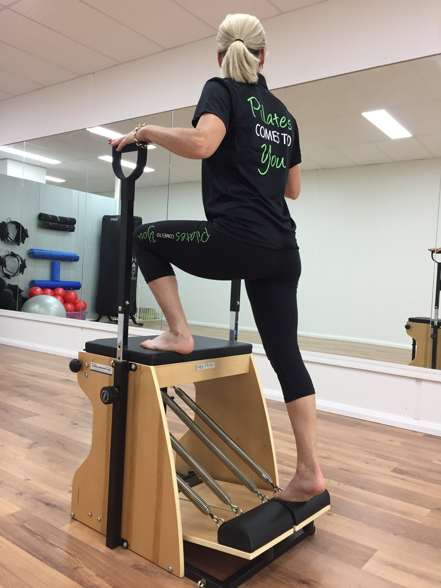 Step-up exercise on the Pilates chair, instructor wearing a Pilates Comes To You shirt